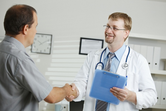 Medical office - middle-aged male doctor greeting patient, shaking hands.